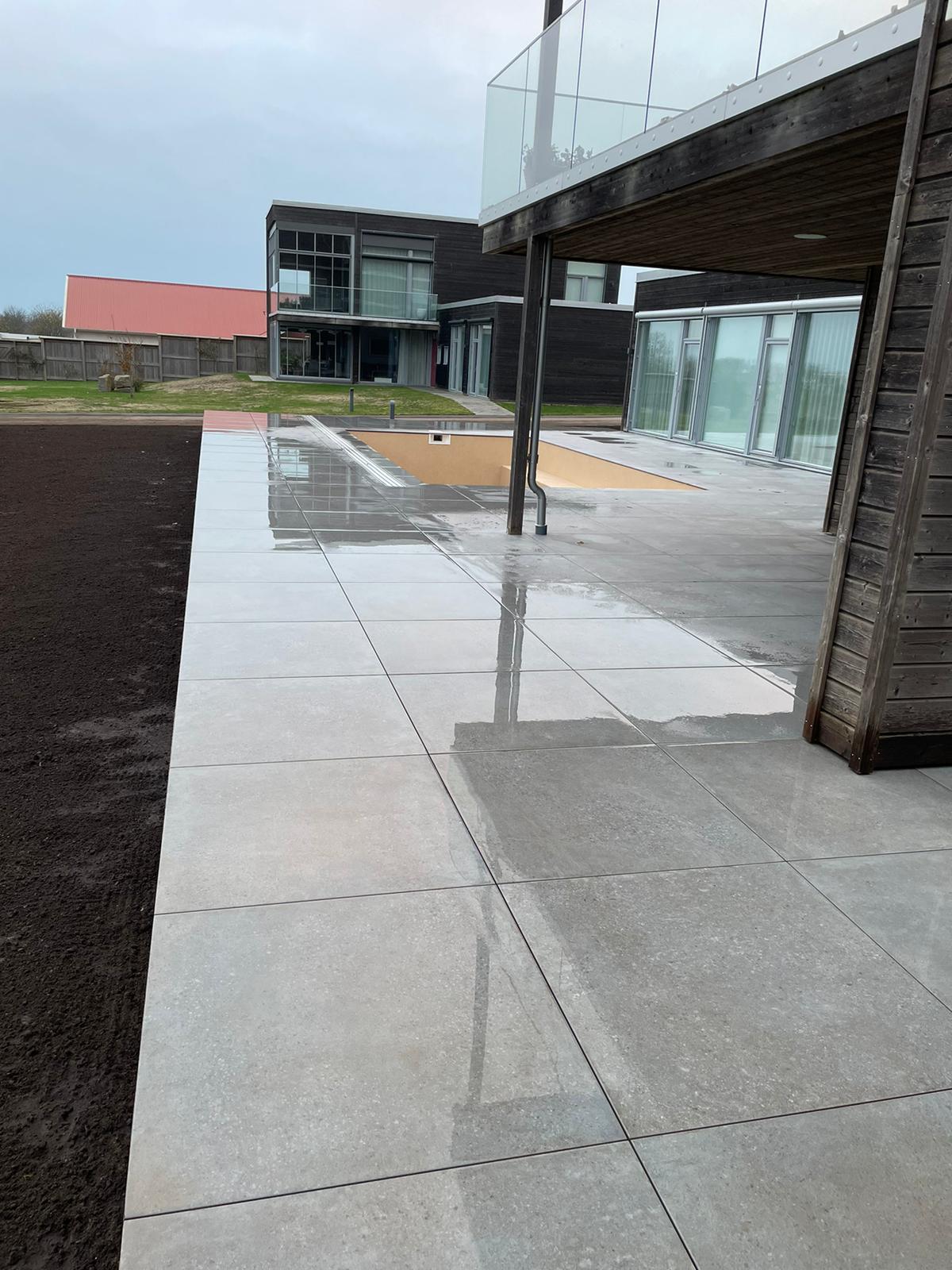 Nylagd stenläggning med reflektioner av en byggnad och himmel, ett exempel på stenläggningsprojekt utfört av Thorssons Entreprenad i området omkring Halmstad.