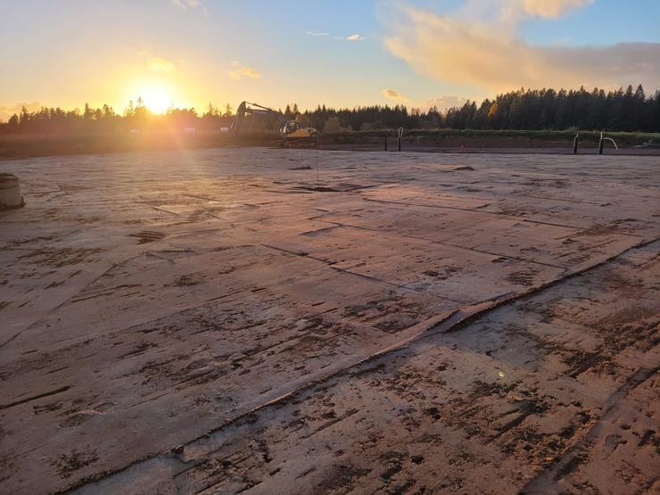 Solnedgången kastar ett mjukt ljus över en stor betongplatta förberedd för vidare konstruktion, ett exempel på Thorssons Entreprenads markarbete i Halmstadregionen.